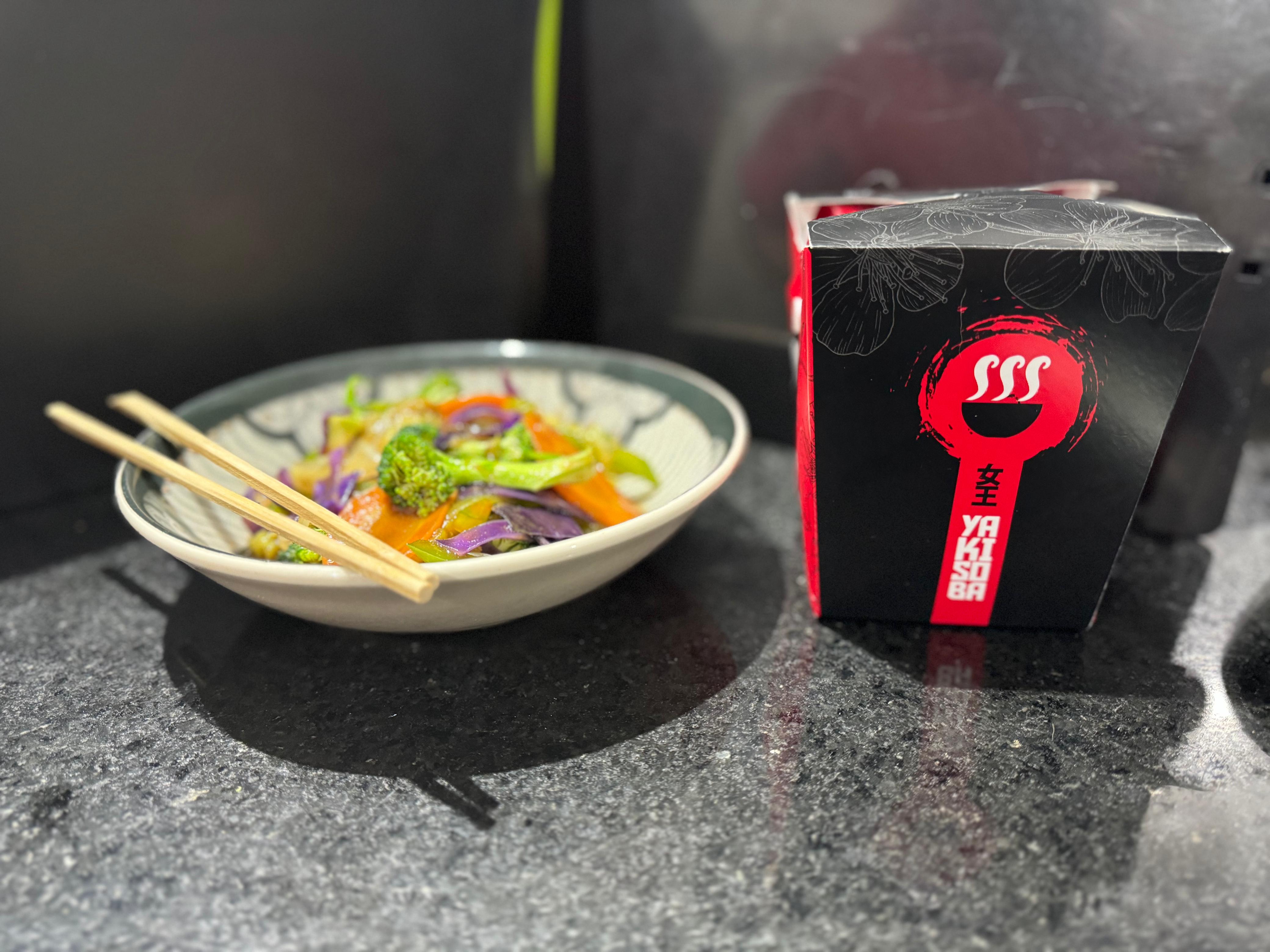 Tigela de yakisoba colorido ao lado de embalagem para delivery MA Oriental